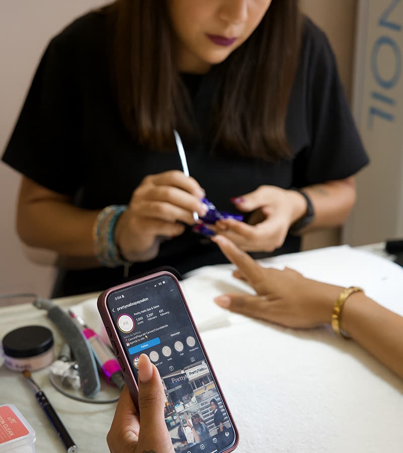 Una manicurista de Pretty Nails trabaja mientras la clienta mira su celular